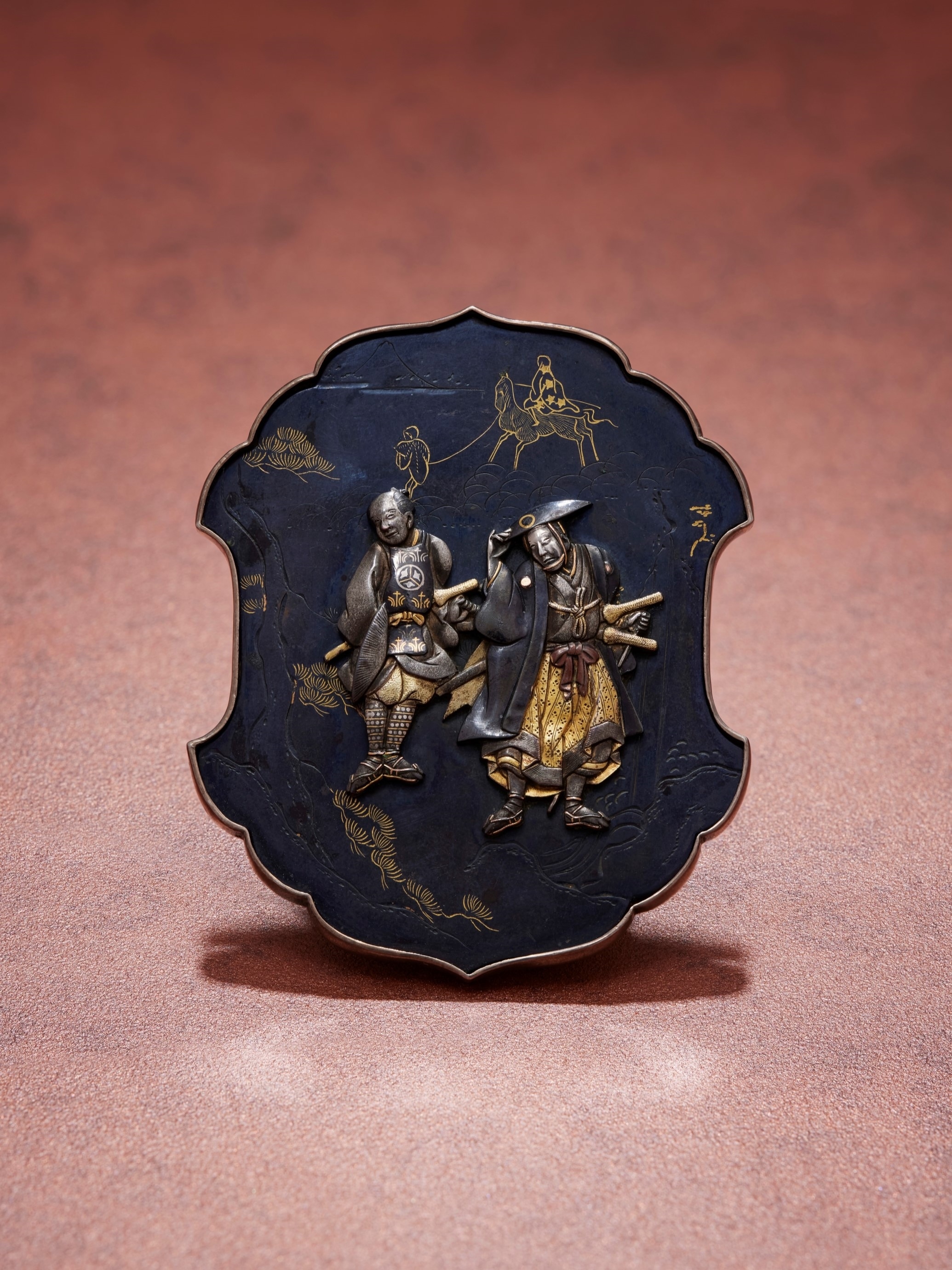 Buckle resembling a sword guard, with an elderly samurai and cane, accompanied by another samurai, Japan, late 1800s. Gold and silver-gilt shakudō, possibly painted with maki-e lacquer. Private Collection. Photo: L'ÉCOLE, School of Jewelry Arts - Benjamin Chelly.